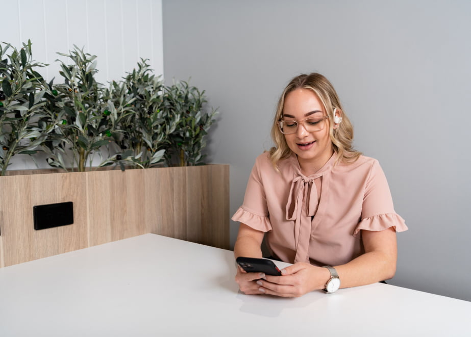 Jenny from Exclaim IT talking to a candidate on her mobile, sitting at a desk with a planter box behind her.